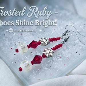 Puede incluir: Pendientes colgantes con dijes de copo de nieve en tono plateado, cuentas de cristal rojo rubí facetado y cuentas blancas iridiscentes en ganchos de metal. El texto Frosted Ruby - Echoes Shine Bright! y Etsy Handmade Jewelry es visible.