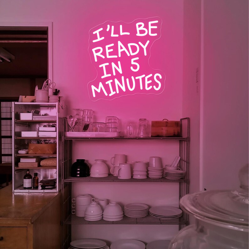 Może przedstawiać: R&oacute;żowy neon z napisem "I'LL BE READY IN 5 MINUTES" wisi na r&oacute;żowej ścianie. Poniżej znajduje się metalowa p&oacute;łka z naczyniami. Po lewej stronie znajduje się drewniana p&oacute;łka z r&oacute;żnymi przedmiotami.