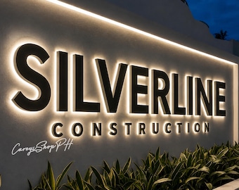Op de afbeelding: Een wandbord met de zwarte, driedimensionale tekst SILVERLINE CONSTRUCTION met geïntegreerde achtergrondverlichting die een zachte gloed op de lichte muur werpt. De tekst CareyShopPH is zichtbaar in de linkerbenedenhoek.