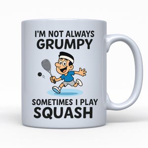 Könnte beinhalten: Weiße Keramiktasse mit einer Cartoon-Illustration einer Person beim Squashspielen. Der Text auf der Tasse lautet "I'M NOT ALWAYS GRUMPY SOMETIMES I PLAY SQUASH" in schwarzer Schrift. Die Person trägt ein blaues Hemd und ein weißes Stirnband.