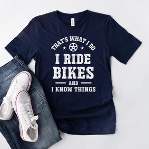 May include: Navy blue t-shirt with white text that reads "That's what I do I ride bikes and I know things". The text is in a distressed font and includes a small bicycle wheel graphic.