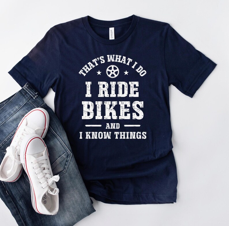 May include: Navy blue t-shirt with white text that reads "That's what I do I ride bikes and I know things". The text is in a distressed font and includes a small bicycle wheel graphic.