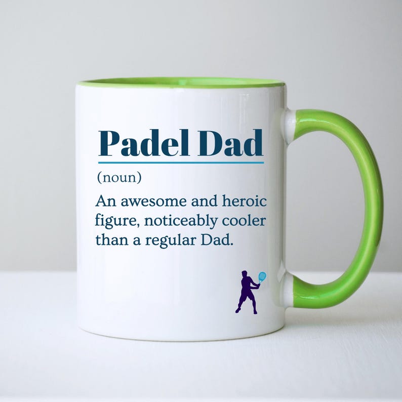 May include: White ceramic mug with a green handle and interior rim. The mug features the text "Padel Dad" in blue, along with a definition and a silhouette of a person playing padel.