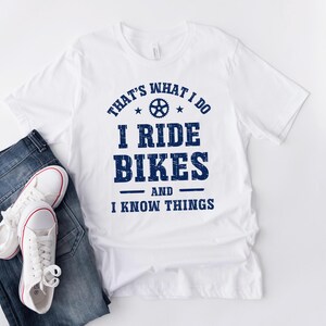 May include: White t-shirt with blue text that reads "That's what I do I ride bikes and I know things". The text is in a distressed font and includes a small bicycle gear graphic.