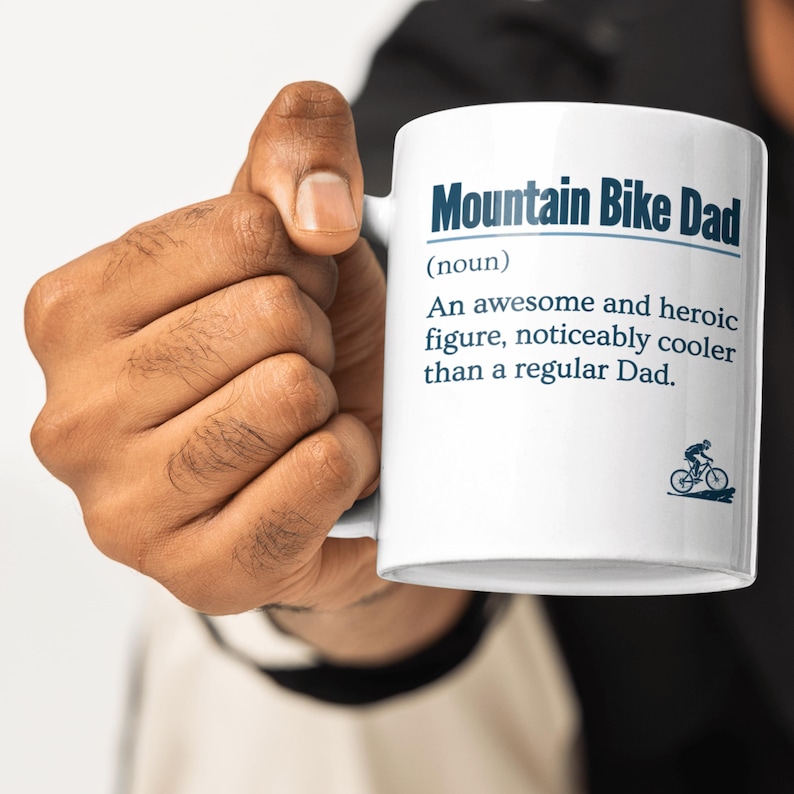 May include: White ceramic mug with a black and blue design. The mug reads "Mountain Bike Dad (noun) An awesome and heroic figure, noticeably cooler than a regular Dad."