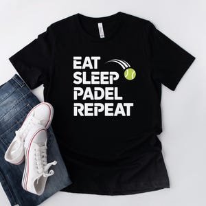 May include: Black t-shirt with white text that reads "Eat Sleep Padel Repeat" and a white tennis ball graphic.