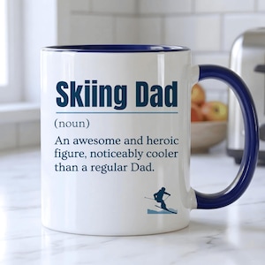 Peut inclure: Mug en céramique blanche avec intérieur et anse bleus. Le mug affiche le texte "Skiing Dad" en bleu, avec une définition et un graphique de skieur. Un cadeau humoristique pour un papa qui aime le ski.