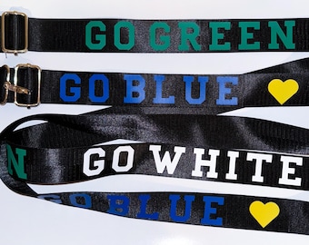 May include: Black lanyards with gold-colored metal clasps and the phrases "GO GREEN", "GO BLUE", and "GO WHITE" printed in green, blue, and white block letters. A yellow heart graphic is also present.