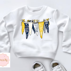 May include: White sweatshirt with a navy blue and yellow pennant banner design. The pennants have the words "Game Day", "Wolverines", "Go Blue", "Fight Blue", and "Fight  'em" printed on them.
