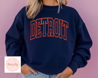 May include: A navy blue sweatshirt with the word "DETROIT" printed in orange on the front.