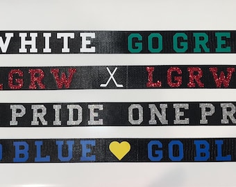 May include: Four black ribbon banners with white, green, red, and blue text. The text on the banners reads "GO WHITE GO GREEN", "X LGRW X LGRW X", "ONE PRIDE ONE PRIDE", and "GO BLUE GO BLUE".