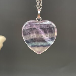 Puede incluir: Colgante en forma de coraz&oacute;n hecho de piedra transl&uacute;cida, con tonos de morado, blanco y azul. Cuelga de una delicada cadena de plata. Los patrones naturales de la piedra crean un dise&ntilde;o &uacute;nico y llamativo. Una joya.