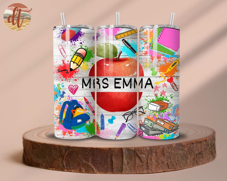 May include: Three stainless steel tumblers with colourful designs featuring a red apple, pencils, and other school supplies. The tumblers have a white background with black text that reads "Mrs. Emma".