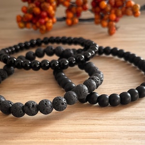 Könnte beinhalten: Drei schwarze Perlenarmbänder, zwei mit schwarzen Lavasteinen und eines mit glatten schwarzen Perlen.