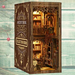 Op de afbeelding: Een houten diorama in de vorm van een open boek met de tekst "Ancient Book" en "Collection Room". De binnenkant toont een gedetailleerde miniatuur bibliotheek met planken, een ladder en warme verlichting, wat een gezellige scène creëert.