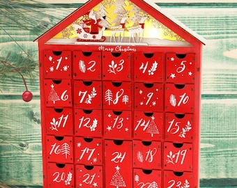 Peut inclure: Un calendrier de l'Avent de Noël en bois rouge en forme de maison, avec 24 tiroirs numérotés. Le haut présente une scène de Père Noël et de rennes avec les mots "Merry Christmas". Chaque tiroir est décoré de motifs festifs.