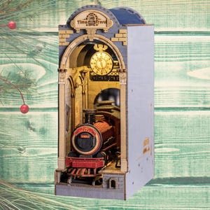 May include: A wooden diorama featuring a train engine inside a building with an arched doorway. The diorama has a clock and the words "Time Travel" at the top. The train is red and black. The background is a green wooden surface.