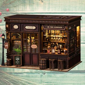 Op de afbeelding: Een miniatuur houten taverne met een donkerbruin exterieur, met een bord met de tekst "The Hidden Tavern in the Corner". Het interieur is verlicht en toont flessen en bardetails. Een klein bordje leest "Wine Shop".