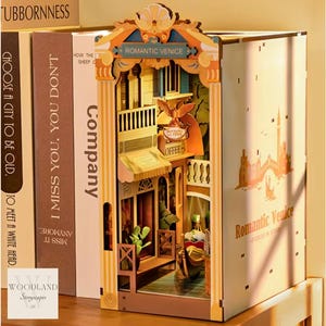 Op de afbeelding: Een houten model van een gebouw met een bord waarop "Romantic Venice" staat. Het model is geschilderd in tinten bruin, crème en goud. Het gebouw heeft een balkon en een winkel met een bord waarop "Coffee" staat.