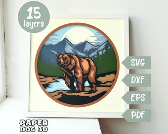 Puede incluir: Un diseño de papercraft de 15 capas que representa un oso marrón de pie en un paisaje de montaña con un lago azul. El diseño está en un círculo con un borde marrón y un fondo blanco. La imagen incluye el texto "PAPER DOG 3D" y "15 capas".