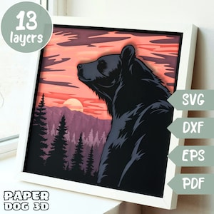 Puede incluir: Un modelo de papercraft de 13 capas que representa un oso negro de pie en un bosque al atardecer. El oso mira hacia la derecha y el sol se pone detrás de una cordillera. El modelo está enmarcado en un marco blanco.