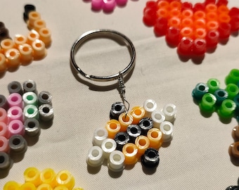 May include: A keychain with a variety of colorful heart-shaped bead designs. The keychain features a silver key ring and a small charm with a white, orange, and black bead design.