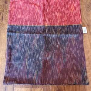 May include: A red and black patterned pillow with a gold stripe. The pillow has a label that says "Handwoven"