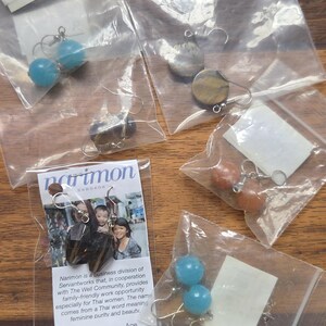 May include: Four small bags of earrings. Each bag contains a pair of earrings with different colored stones. The earrings are made by Narimon, a business division of Servantworks in cooperation with The Well Community, Thailand. The text on the bag reads: "Narimon is a business division of Servantworks that, in cooperation with The Well Community, provides family-friendly work opportunity especially for Thai women. The name comes from a Thai word meaning feminine purity and beauty. Made by A member of The Well, Thailand."