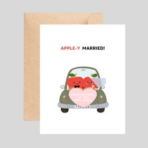 May include: A wedding greeting card with the text "APPLE-Y MARRIED!" shows a cartoon car with two apple characters inside. One apple wears a bow tie, the other a veil. A pink heart-shaped sign reads "Congratulations to the happy couple" and "Forever".