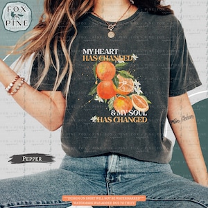 May include: A dark gray t-shirt with a graphic of oranges and white flowers. The text "My heart has changed & my soul has changed" is printed on the shirt.