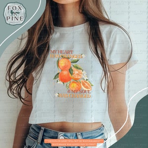 May include: A white crop top with the text "My heart has changed & my soul has changed" printed in orange and brown. The text is surrounded by a graphic of orange slices and leaves.