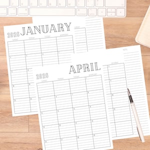 Pode incluir: São exibidas duas páginas de calendário mensal sem data de 2026, janeiro e abril. Os calendários são impressos em tinta preta em papel branco. Uma caneta prateada repousa sobre o calendário de abril. Um teclado de computador é visível ao fundo.