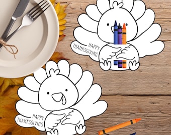 Puede incluir: Dos páginas para colorear con forma de pavo blanco con el texto "Happy Thanksgiving". Un pavo sostiene crayones. Un plato con tenedor y cuchillo está en la esquina superior izquierda. Los crayones están esparcidos sobre una superficie de madera.
