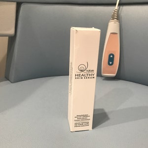 May include: White box with a black and white logo of a snail with the text "nature cosmeceuticals" and "HEALTHY SKIN SERUM".