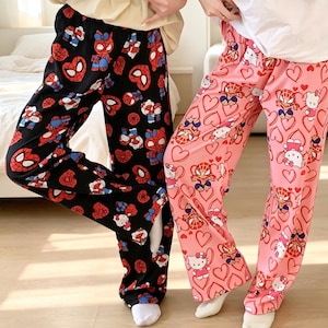 May include: Two pairs of lounge pants featuring a repeating pattern of cartoon characters and hearts. One pair is black with red and blue character motifs, while the other is light pink with red heart outlines and character graphics throughout.