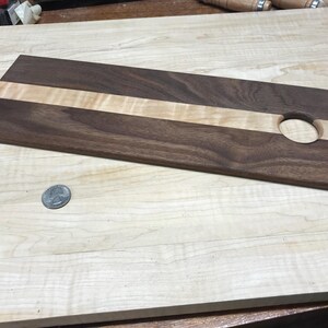 Op de afbeelding: Een rechthoekig houten serveerplank met een donkerbruine walnoot buitenkant en een lichtgekleurde esdoorn streep in het midden. Het heeft een cirkelvormig gat aan &eacute;&eacute;n uiteinde. De plank is ongeveer 40 cm lang.