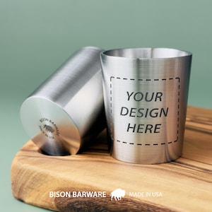 May include: Two stainless steel cups, one with the text "BISON BARWARE MADE IN USA" and the other with the text "YOUR DESIGN HERE" in a dashed box.