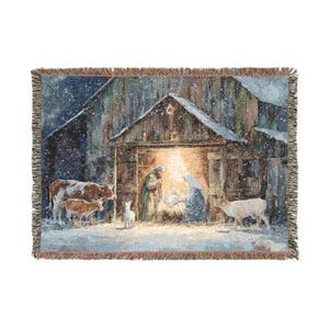 Könnte beinhalten: Gewebte Decke mit einer Darstellung der Geburt Christi in einer verschneiten Scheune. Das Kunstwerk zeigt einen leuchtenden Stall, Figuren und Tiere mit einem Fransenrand. Die Farbpalette umfasst Blau-, Braun- und Weißtöne.