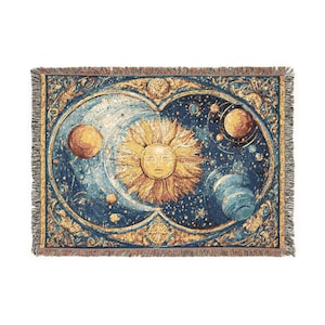 May include: A woven tapestry blanket featuring a celestial design. The artwork depicts a sun with a face, planets, and stars against a blue background. The blanket has a fringed edge and a detailed border with gold and cream accents.
