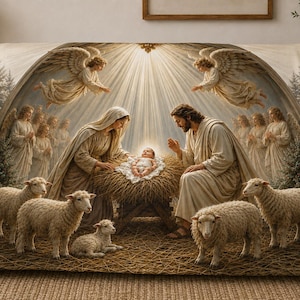 May include: A soft throw blanket featuring a nativity scene with a baby in a manger, Mary and Joseph, and several sheep. Above them, angels are depicted in a bright, glowing light. The scene is framed by evergreen trees and straw.