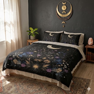 May include: A black duvet cover and two matching pillowcases featuring a celestial and botanical print with gold crescent moons, blue and purple wildflowers, and yellow sunburst motifs. The bedding set is displayed on a bed with a light-colored skirt.