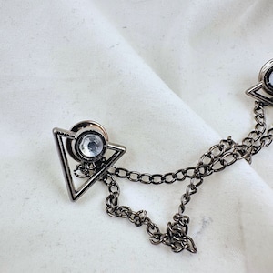 May include: A silver chain with two triangular clasps, each featuring a clear rhinestone. The clasps are connected by a silver chain.