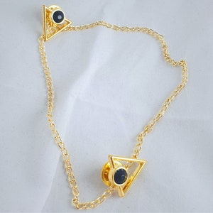 May include: A gold chain with two triangular pendants. Each pendant has a black circle in the center.