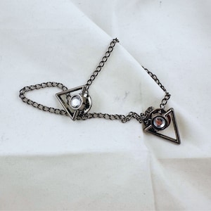 May include: A silver chain with two triangle-shaped charms, each with a clear rhinestone in the center.