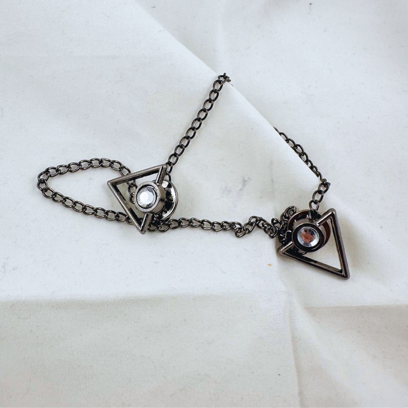 May include: A silver chain with two triangle-shaped charms, each with a clear rhinestone in the center.