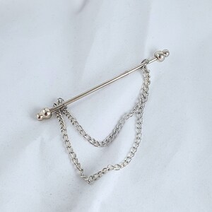 Op de afbeelding: Zilveren stropdasgesp met een dubbele ketting. De ketting is bevestigd aan een zilveren staaf met twee ronde uiteinden.