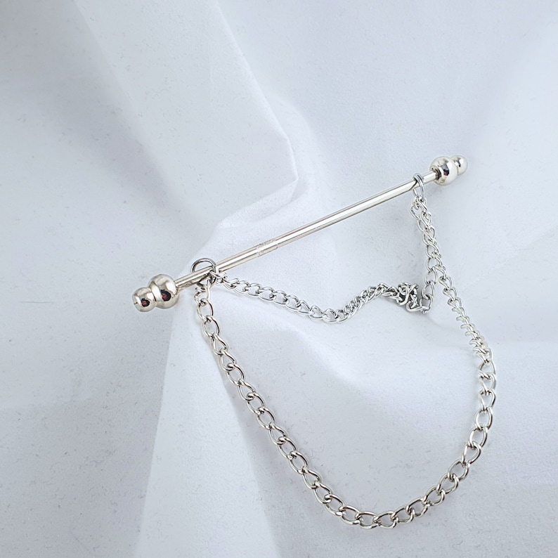 Op de afbeelding: Een zilveren stropdasgesp met een ketting eraan. De ketting heeft een decoratief ontwerp.