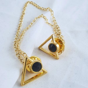 May include: A gold chain with two triangular pendants. Each pendant has a black gemstone in the center.
