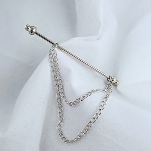 Op de afbeelding: Zilveren stropdasgesp met een ketting eraan. De ketting is dubbel gelegd en heeft aan elk uiteinde een zilveren bol.