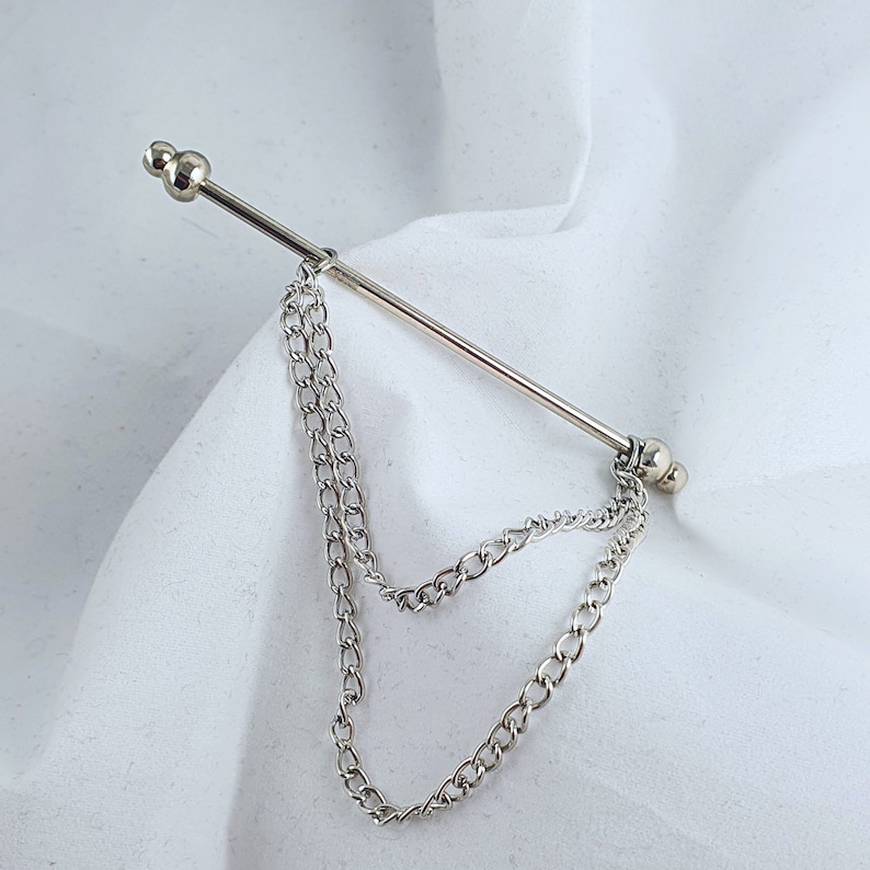 Op de afbeelding: Zilveren stropdasgesp met een ketting eraan. De ketting is dubbel gelegd en heeft aan elk uiteinde een zilveren bol.